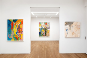 Art gallery interior with three colorful abstract paintings on white walls and a wooden floor.