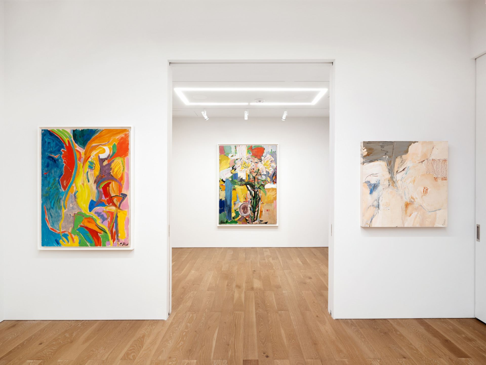 Art gallery interior with three colorful abstract paintings on white walls and a wooden floor.