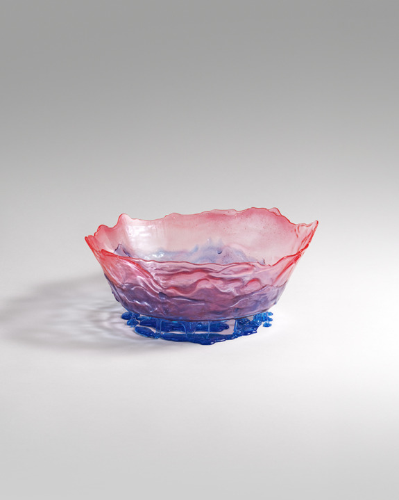A vibrant pink and blue glass bowl with a textured, wavy rim and intricate base on a soft gray background.