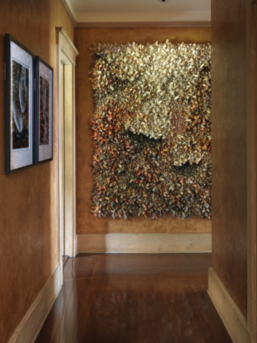 Hallway with textured wall sculpture featuring shades of brown and gold, alongside framed artworks, on a wooden floor.