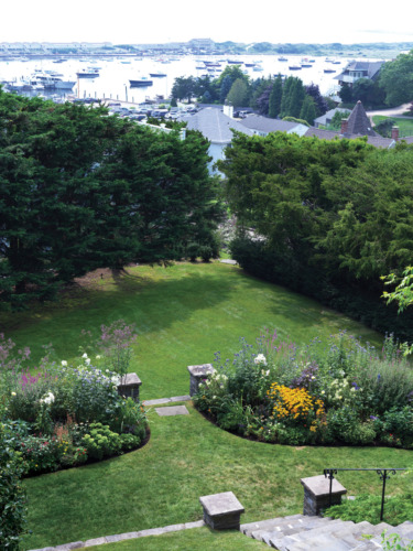 Aerial view of a landscaped garden with stone steps leading to a harbor filled with boats in the background