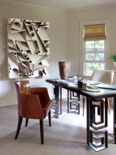 Modern office with abstract wall art, leather chair, elegant desk, large window, and artistic decor in a bright room.