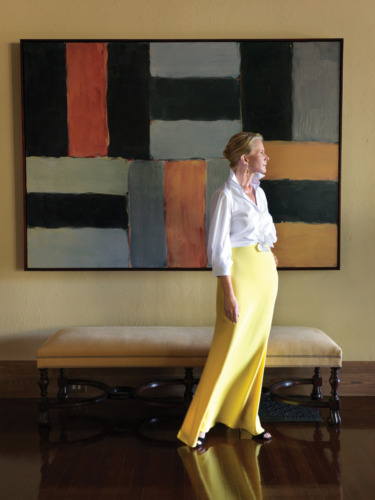 Woman in white blouse and yellow skirt standing by a modern abstract painting and a beige bench.