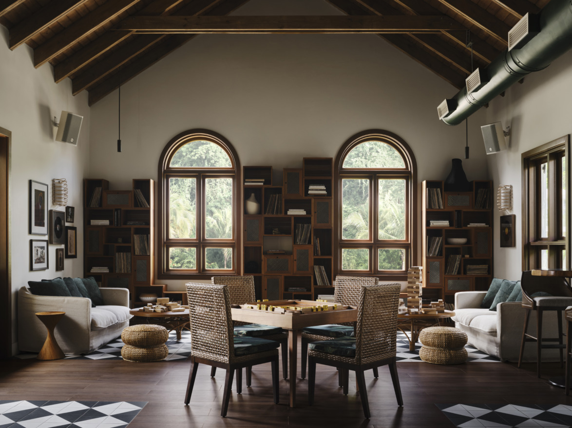 Cozy living room with wooden ceiling, large windows, bookshelves, furniture, and checkered floor tiles.