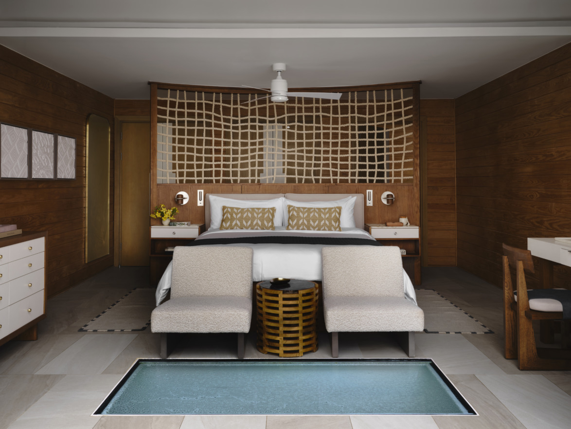 Luxurious hotel room with a large bed, cozy seating, wooden decor, and an ocean view window on the floor.
