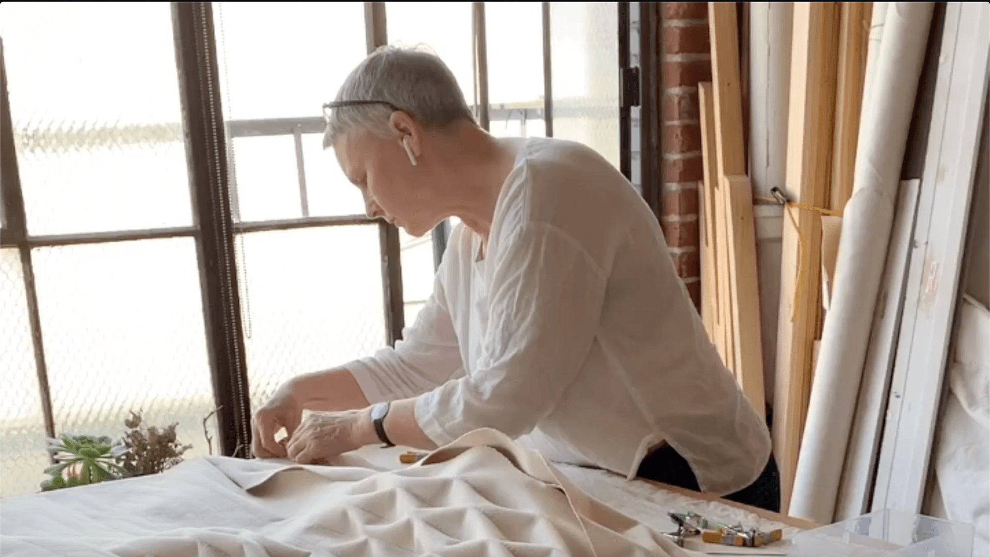Person working on a fabric project in a well-lit studio with large windows.