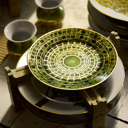 Green patterned ceramic plates stacked on a wooden holder, with cups nearby on a rustic wooden table.