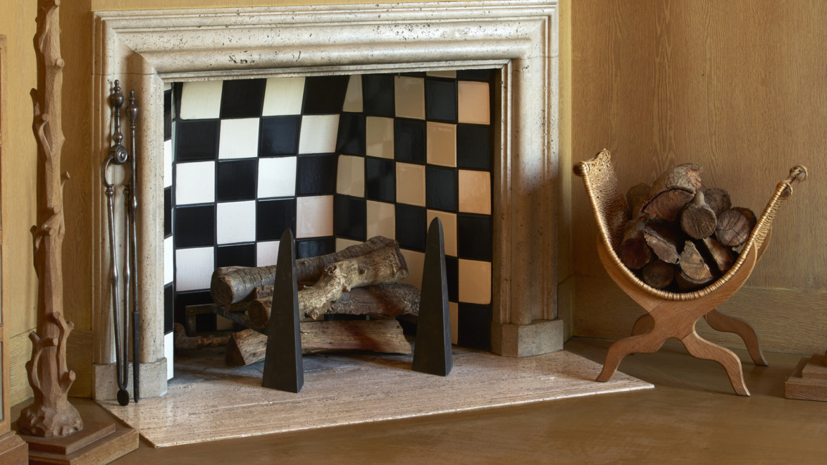 Fireplace with checkerboard tiles, logs stacked inside, and a wicker basket holding firewood on the side.