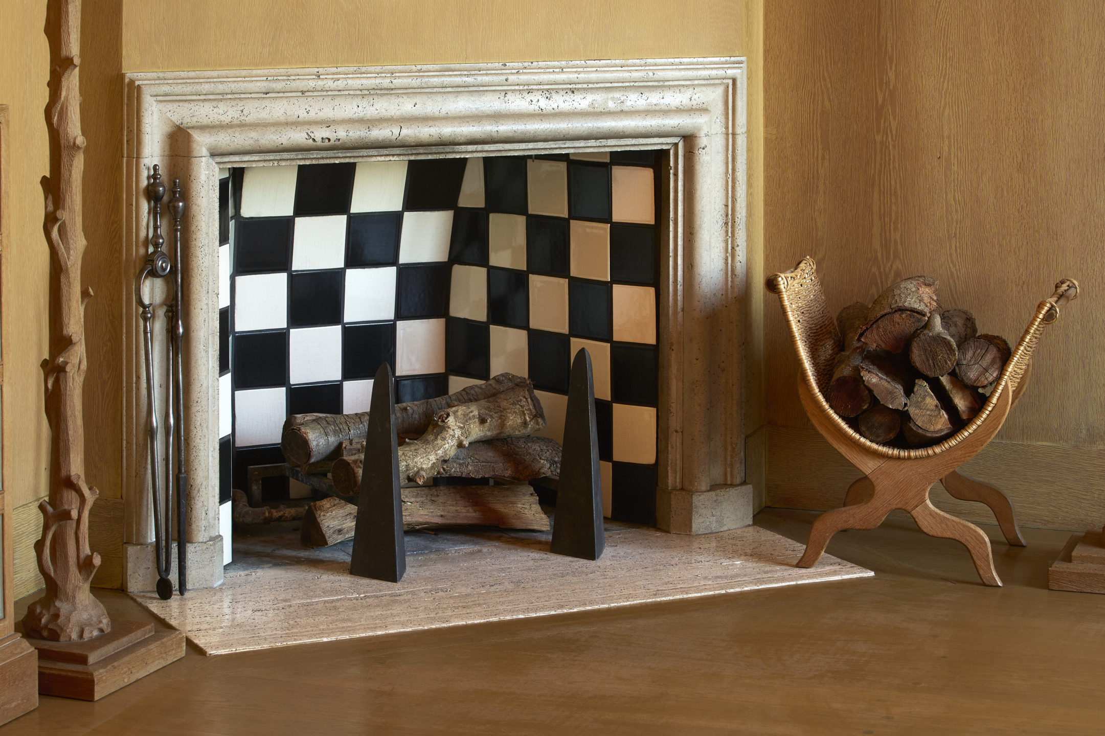 Fireplace with checkerboard tiles, logs stacked inside, and a wicker basket holding firewood on the side.