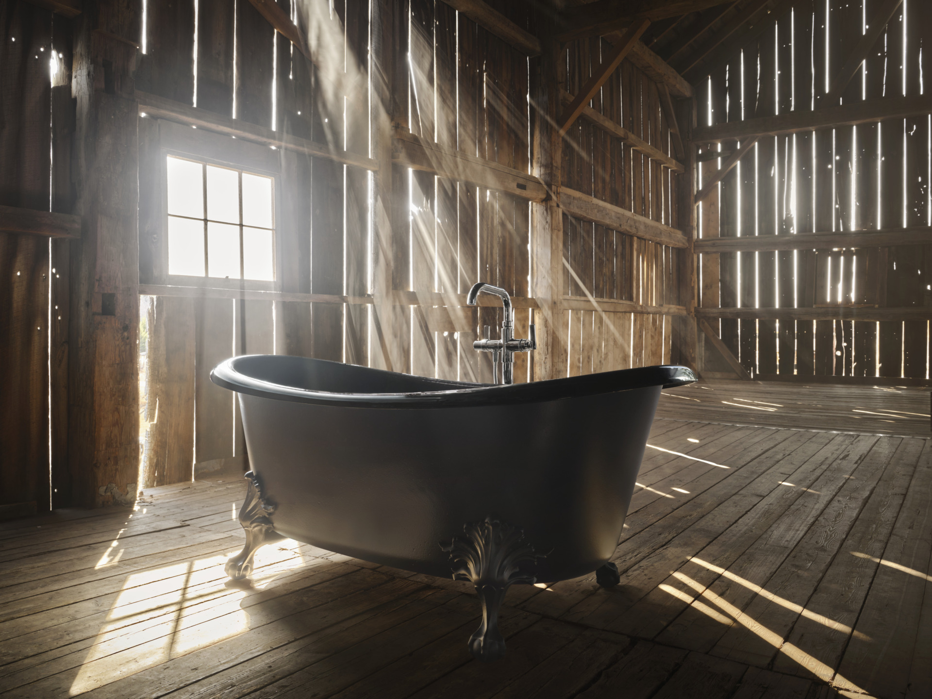 Sunlit vintage clawfoot bathtub in rustic wooden barn interior.