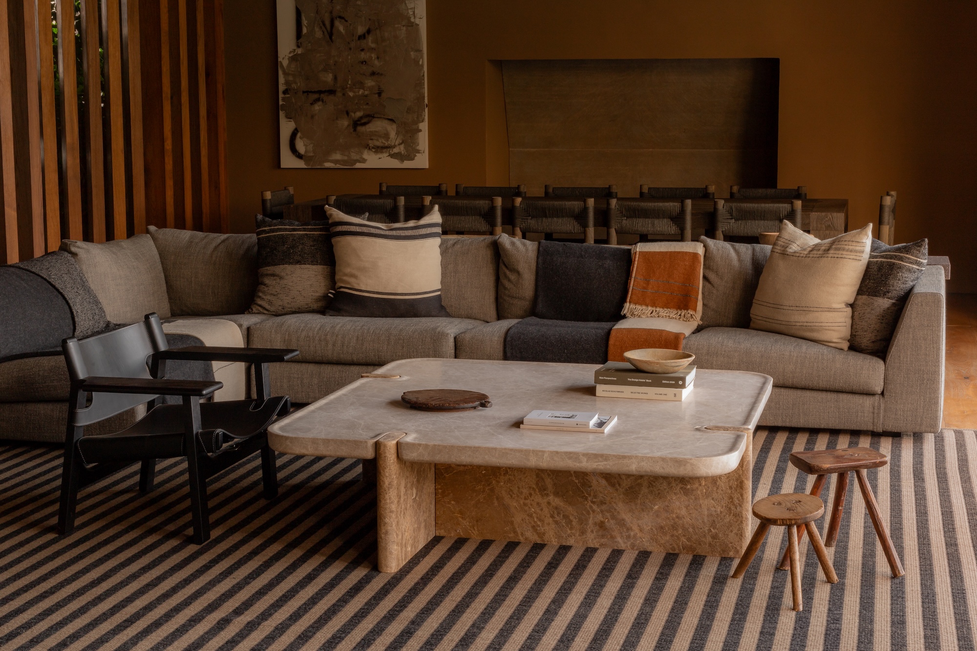 Cozy living room with large sectional sofa, modern armchairs, marble coffee table, and striped rug in neutral tones.