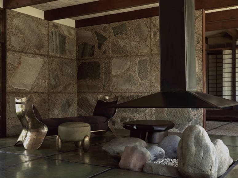 Modern living room with unique stone walls, metallic furniture, and a central hanging fireplace surrounded by large stones.