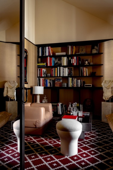 Cozy library with shelves of books, a beige armchair, modern decor, geometric patterned rug, and soft lighting.