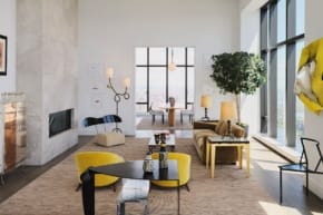 Spacious modern living room with large windows, contemporary furniture, and a neutral color palette featuring yellow accents.
