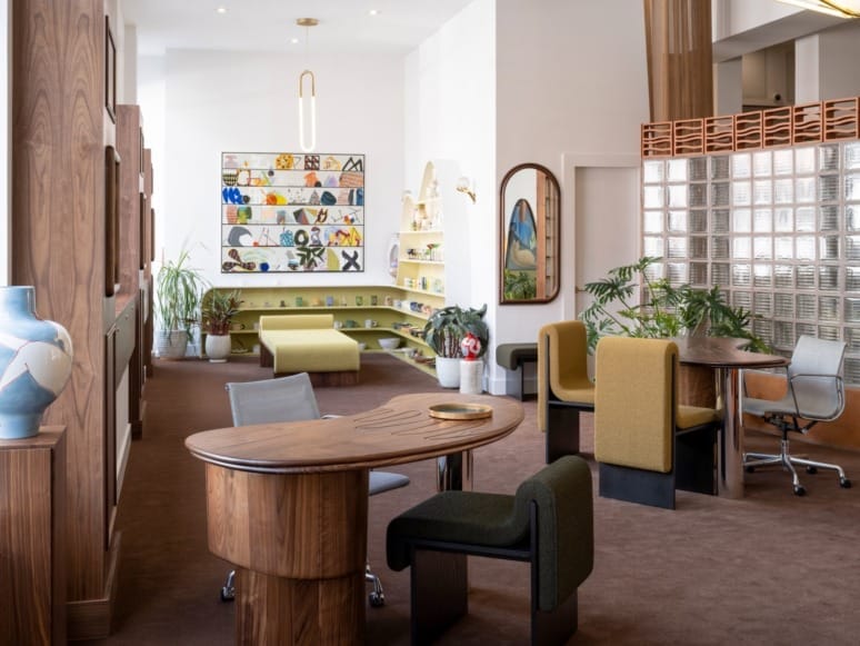 Modern office space with wooden desks, colorful artwork, green seating, plants, and glass block wall for a cozy atmosphere