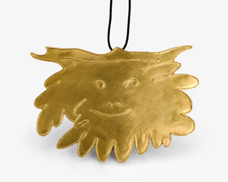 Gold pendant with whimsical face design and black cord on light background.