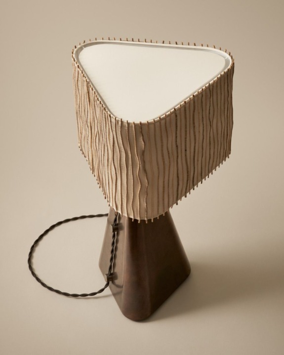 Triangular table lamp with a textured shade and twisted cable on a neutral background.