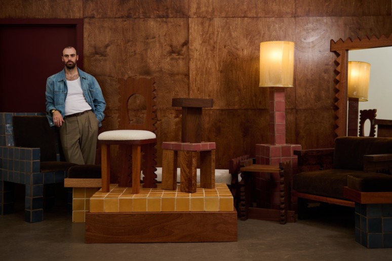 Man standing next to a collection of uniquely designed wooden furniture in a stylish, warmly lit room.
