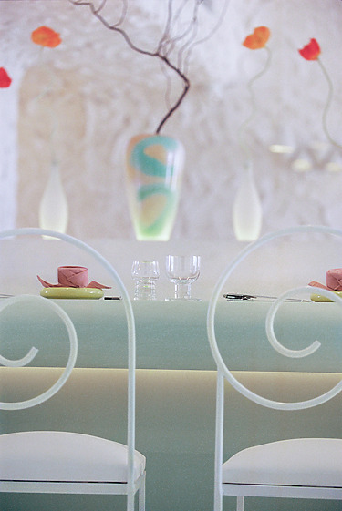 Elegant table setting with pastel chairs, glassware, and a vase with decorative flowers in a softly lit modern space.