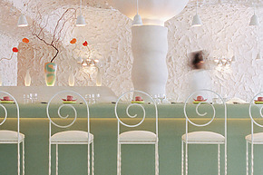 Minimalist bar interior with white high chairs, pastel green counter, decorative plants, and soft lighting.