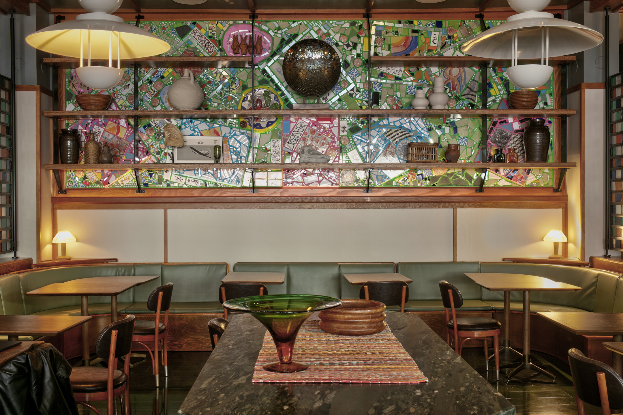 Cozy restaurant interior with colorful mosaic art, wooden shelves, and modern lighting above tables and chairs.