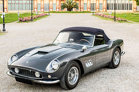 Classic black convertible sports car parked on a gravel driveway in front of an elegant building.