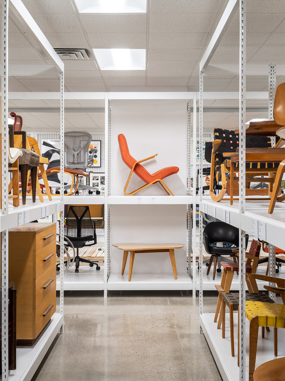 A collection of various designer chairs and tables displayed on white shelves in a well-lit showroom.