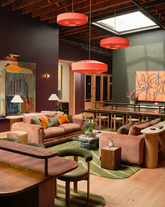 Modern living room with orange sofas, wooden furniture, abstract art, and red pendant lights.