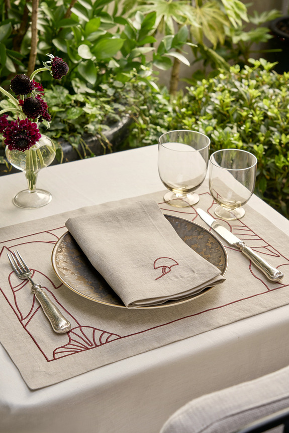 Elegant outdoor table setting with a decorative plate, cloth napkin, cutlery, glasses, and a small vase of flowers.