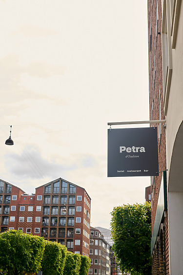 Side view of Petra restaurant sign on brick building with trees and modern apartments in the background.
