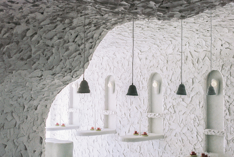 White textured room with arched windows, pendant lights, and small tables with plates arranged in a minimalistic style.