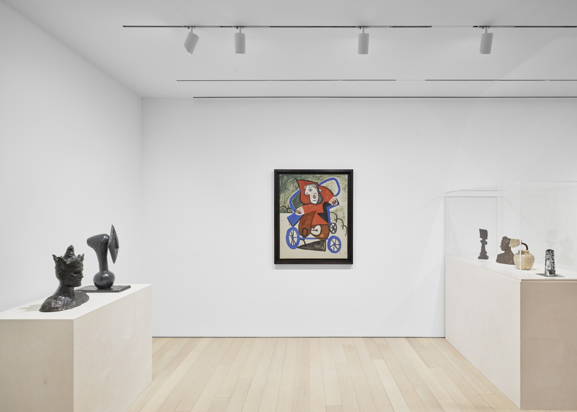 Modern art gallery with sculptures on pedestals and a colorful abstract painting on a white wall under track lighting.