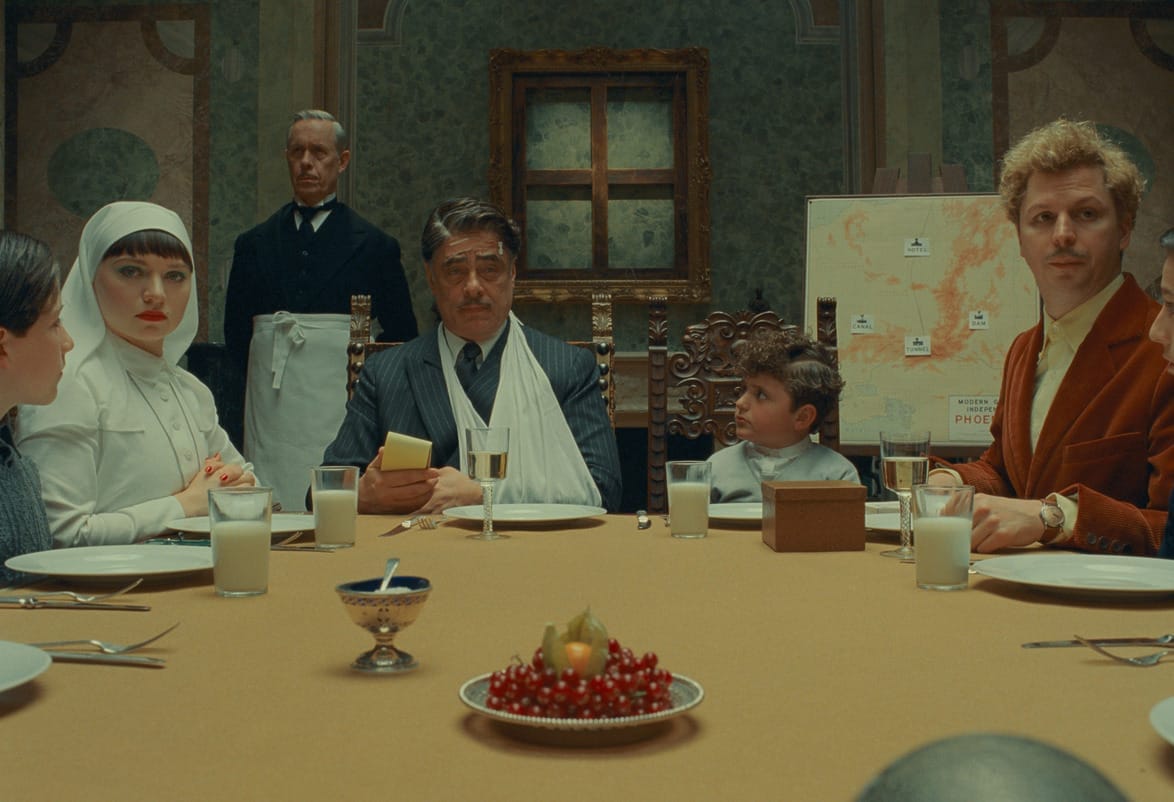A family dining together with a child and a man with an arm sling, surrounded by ornate decor and a map in the background.