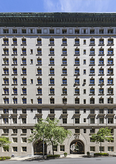 Tall white historic building with many windows, green roof trim, and arched entrances, set against a clear blue sky.