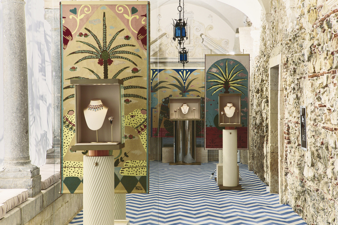 Exhibition space with jewelry displays set against decorative painted panels in a room with a zigzag patterned floor.