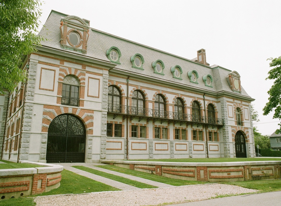 Historic brick and stone building with arched windows and wrought iron balconies, surrounded by grass and pathway.