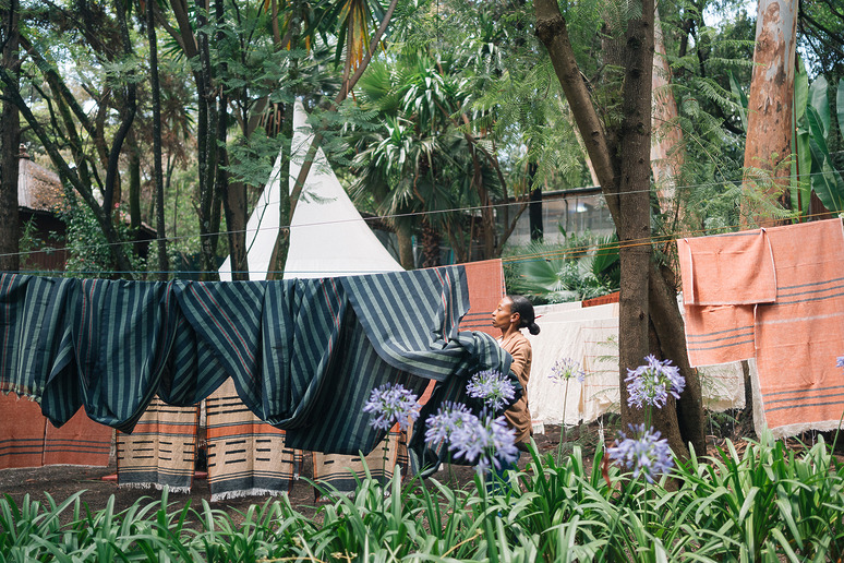 Person hanging striped sheets on a clothesline in a lush garden with blooming flowers.