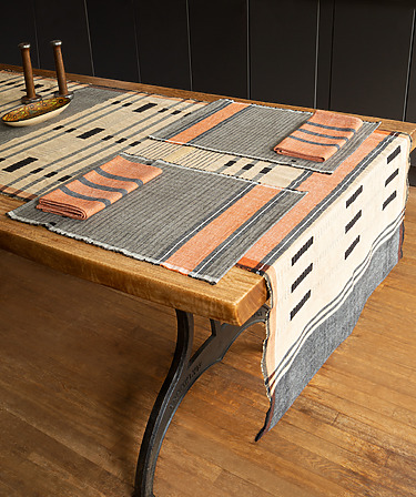 Dining table with patterned table runner and placemats, featuring earthy tones, wooden candle holders in the background.