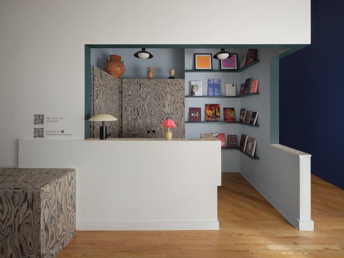 Modern reception area with wood accents, a vase of pink flowers, books on display, and light blue wall highlights.