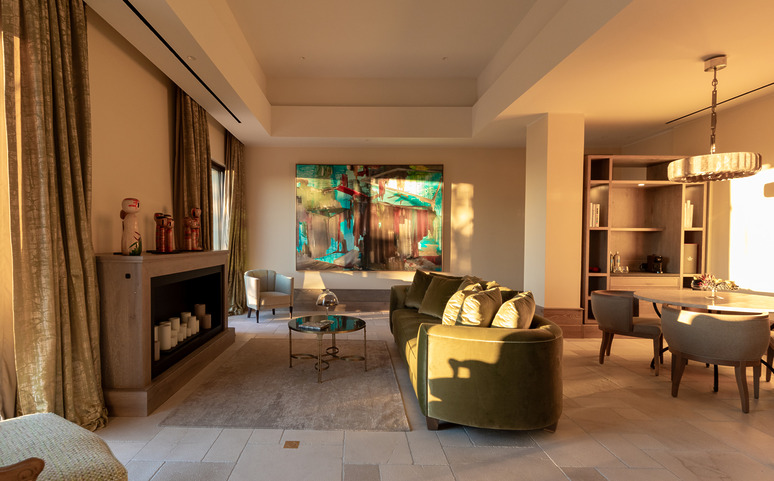 Modern living room with green sofas, colorful artwork on the wall, and sunlight streaming through large windows.