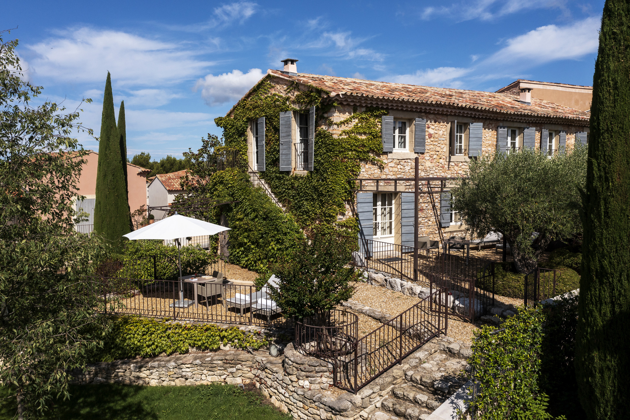 Charming countryside villa with ivy-covered walls, outdoor seating area, and lush garden on a sunny day.