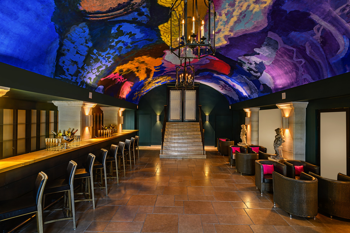Stylish bar with vibrant, artistic ceiling, elegant seating, and chandelier lighting creating a luxurious atmosphere.