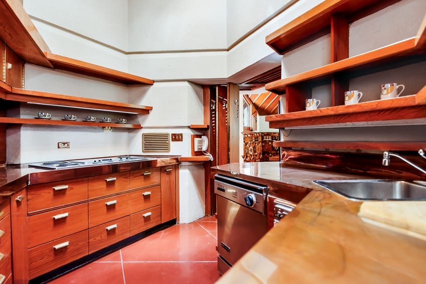 Modern kitchen with wooden cabinets, stainless steel appliances, red tile floor, and open shelving.