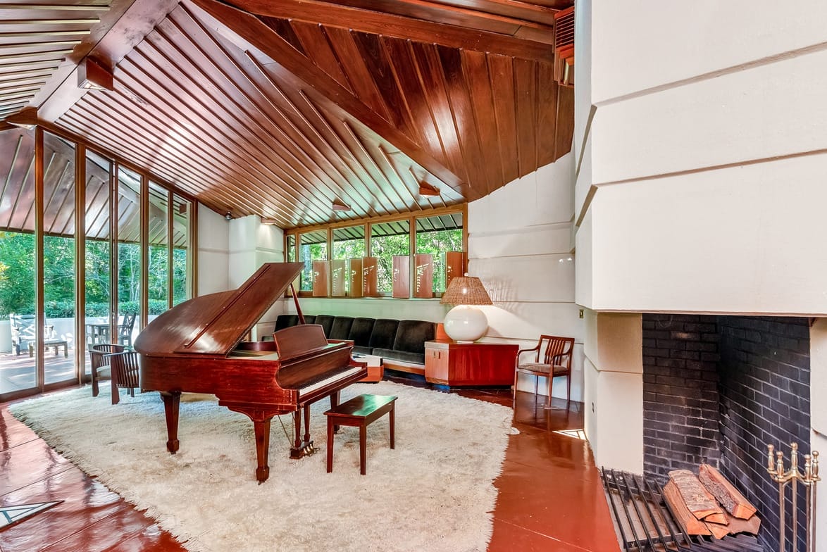 Spacious living room with a grand piano, wooden ceiling, large windows, modern fireplace, and stylish furniture.