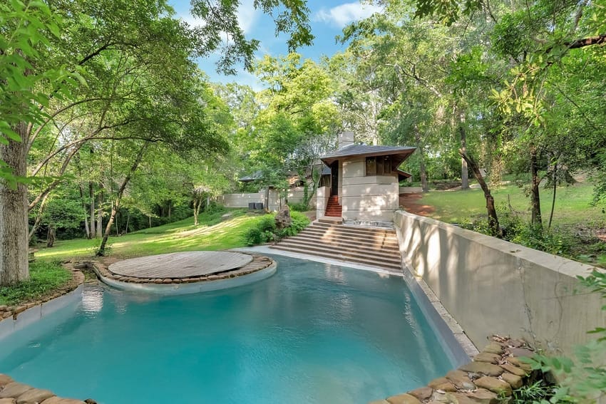 A tranquil backyard with a small round pool, surrounded by lush green trees and a cozy wooden cabin in the background.