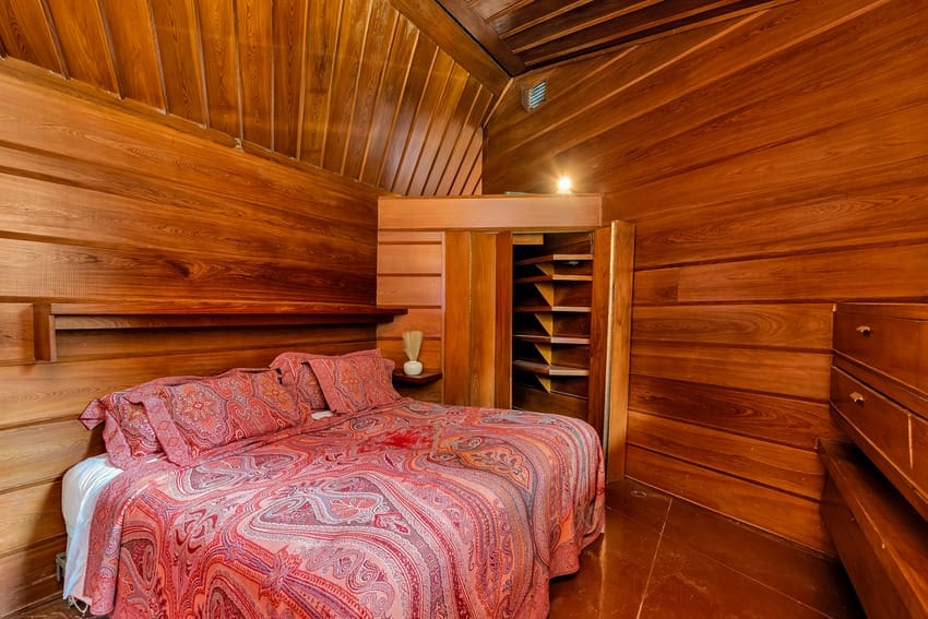 Cozy bedroom with wooden walls, ceiling, and a bed covered in a pink patterned blanket.
