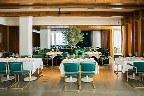 Modern restaurant interior with green chairs, white tablecloths, and a tree centerpiece, featuring wooden accents and natural lighting.