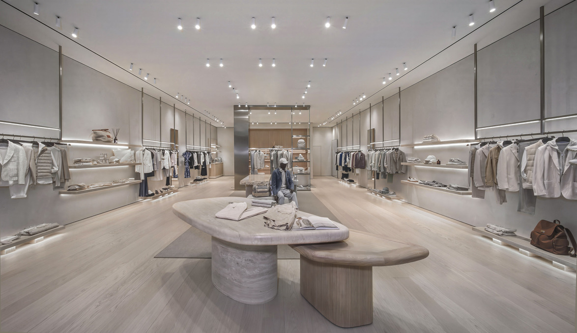 Modern clothing store interior with stylish garments displayed on racks and shelves, featuring neutral tones and elegant lighting.