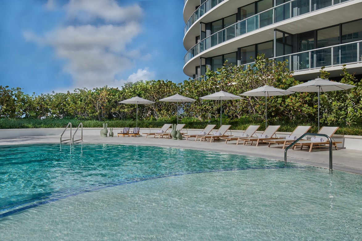 luxurious curved building with poolside loungers and umbrellas under a clear blue sky