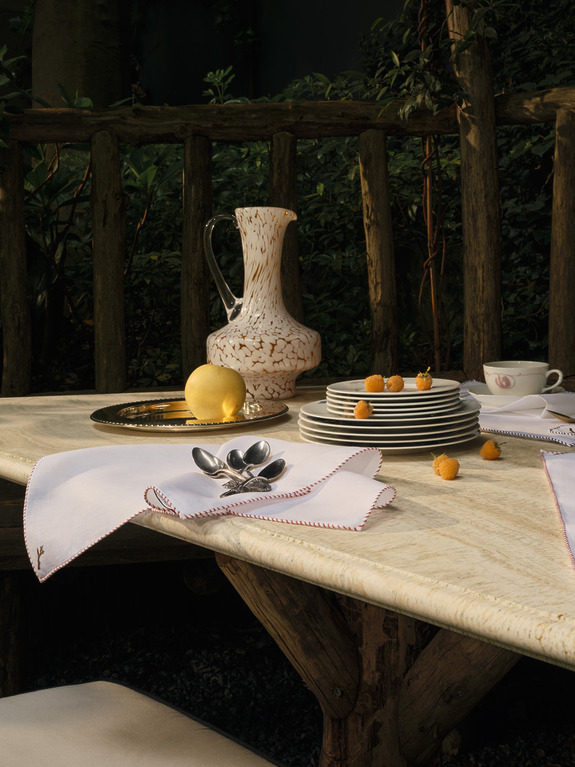 Outdoor table set with plates, napkins, cutlery, a pitcher, a lemon, and small fruits on a rustic wooden surface.